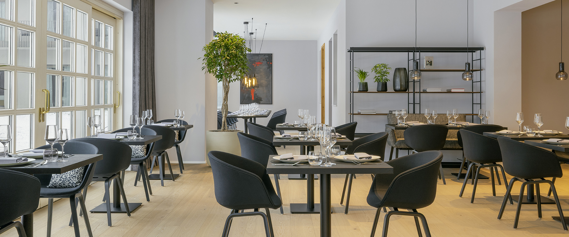 Modernes Hotelrestaurant mit großen Fensterfronten, eleganter Tischdekoration und stilvollen schwarzen Stühlen