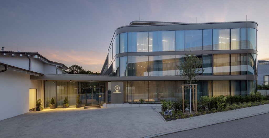 Moderne Hotelfassade mit großen Glasflächen und stilvoller Beleuchtung bei Sonnenuntergang