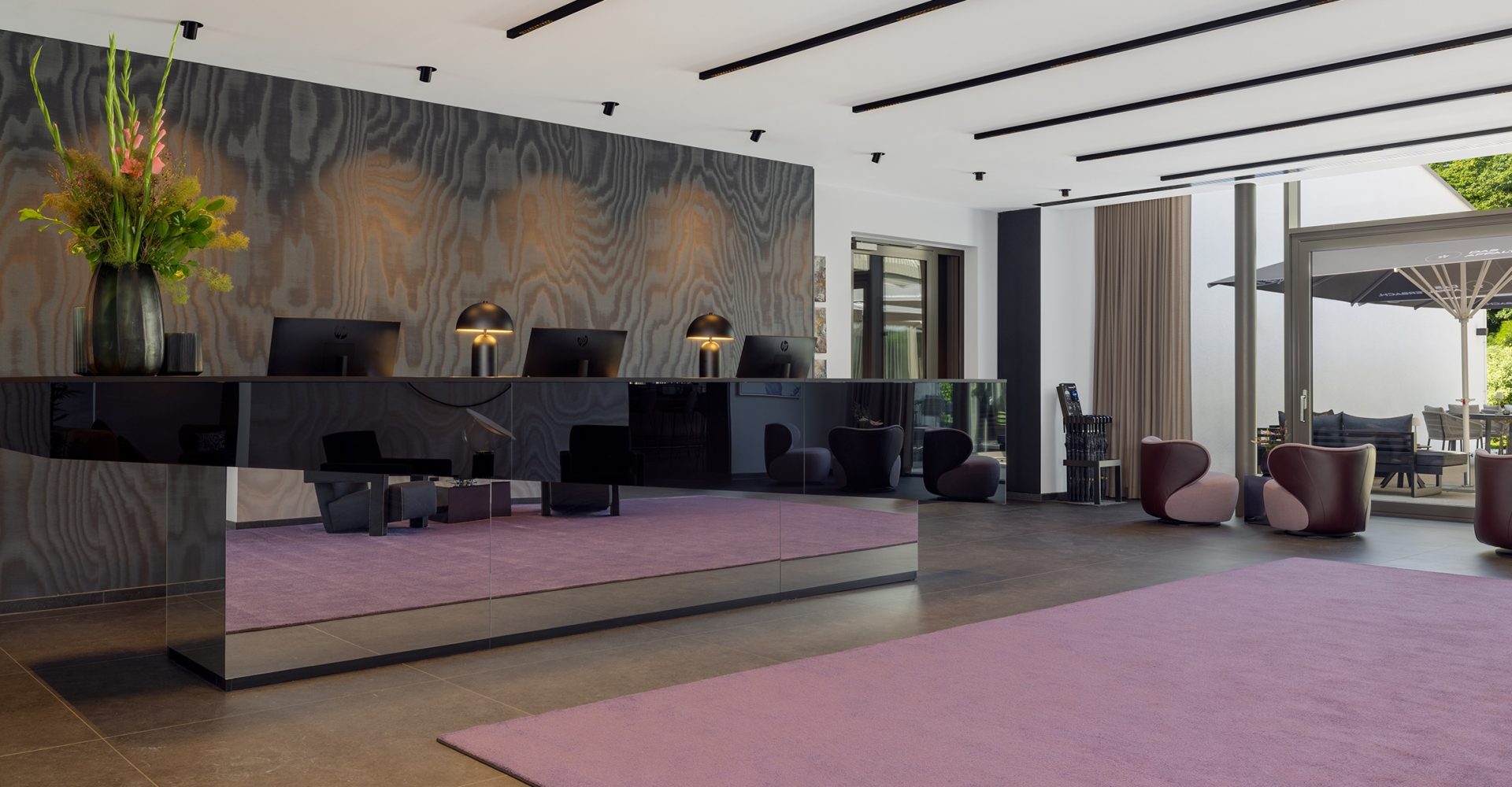 Designorientierte Hotellobby mit schwarzem Empfangstresen, floraler Deko und Lounge-Möbeln