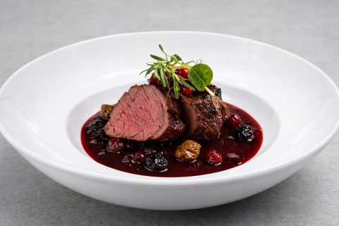 Rosa gebratenes Filet auf weißem Teller in roter Beerensauce