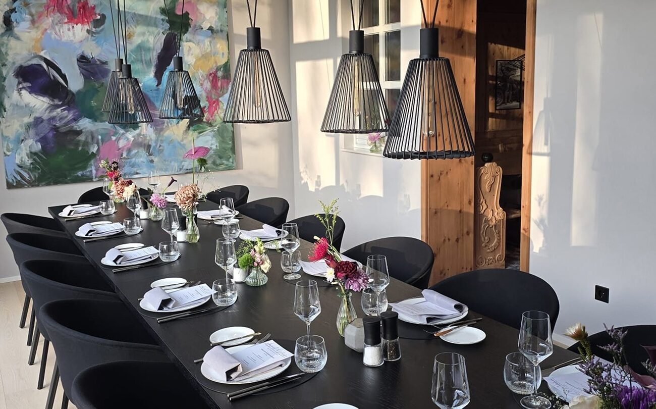 Langer Esstisch, gedeckt mit Gläsern und Blumen, unter Drahtlampen im Restaurant nahe Stuttgart