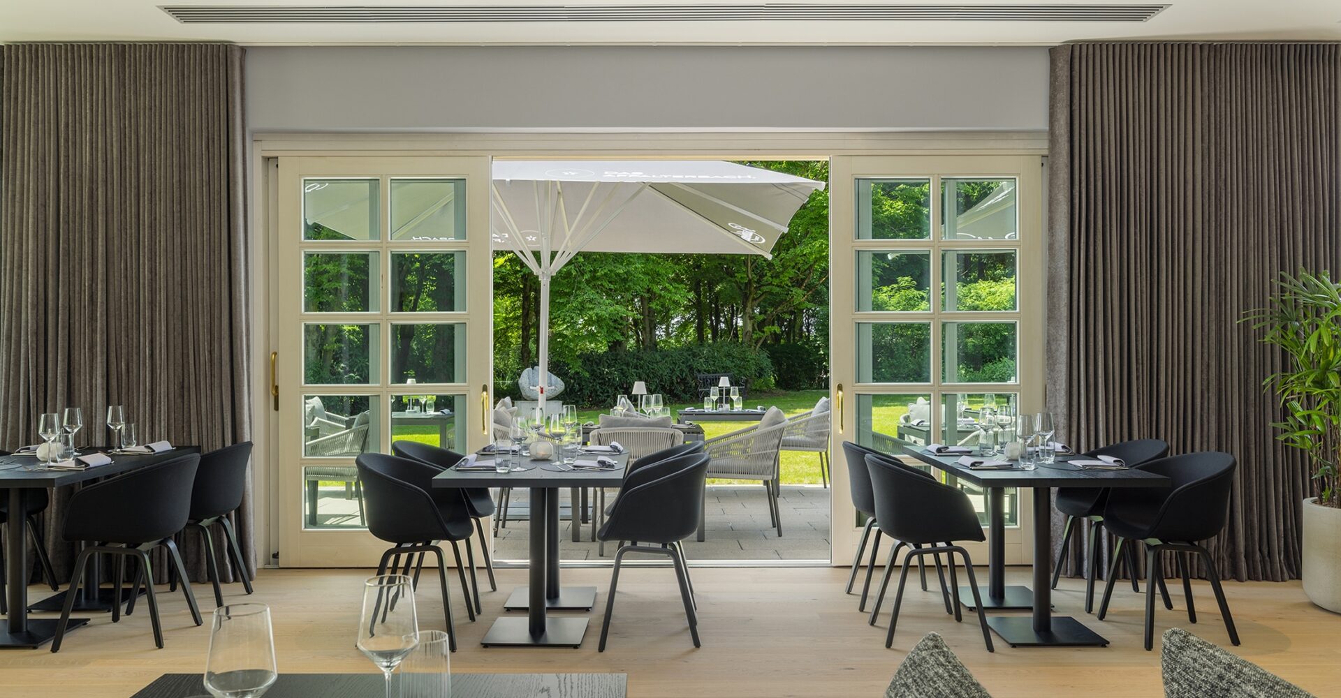 Gedeckte Tische stehen innen vor offener Tür zur grünen Terrasse im Restaurant Affalterbach