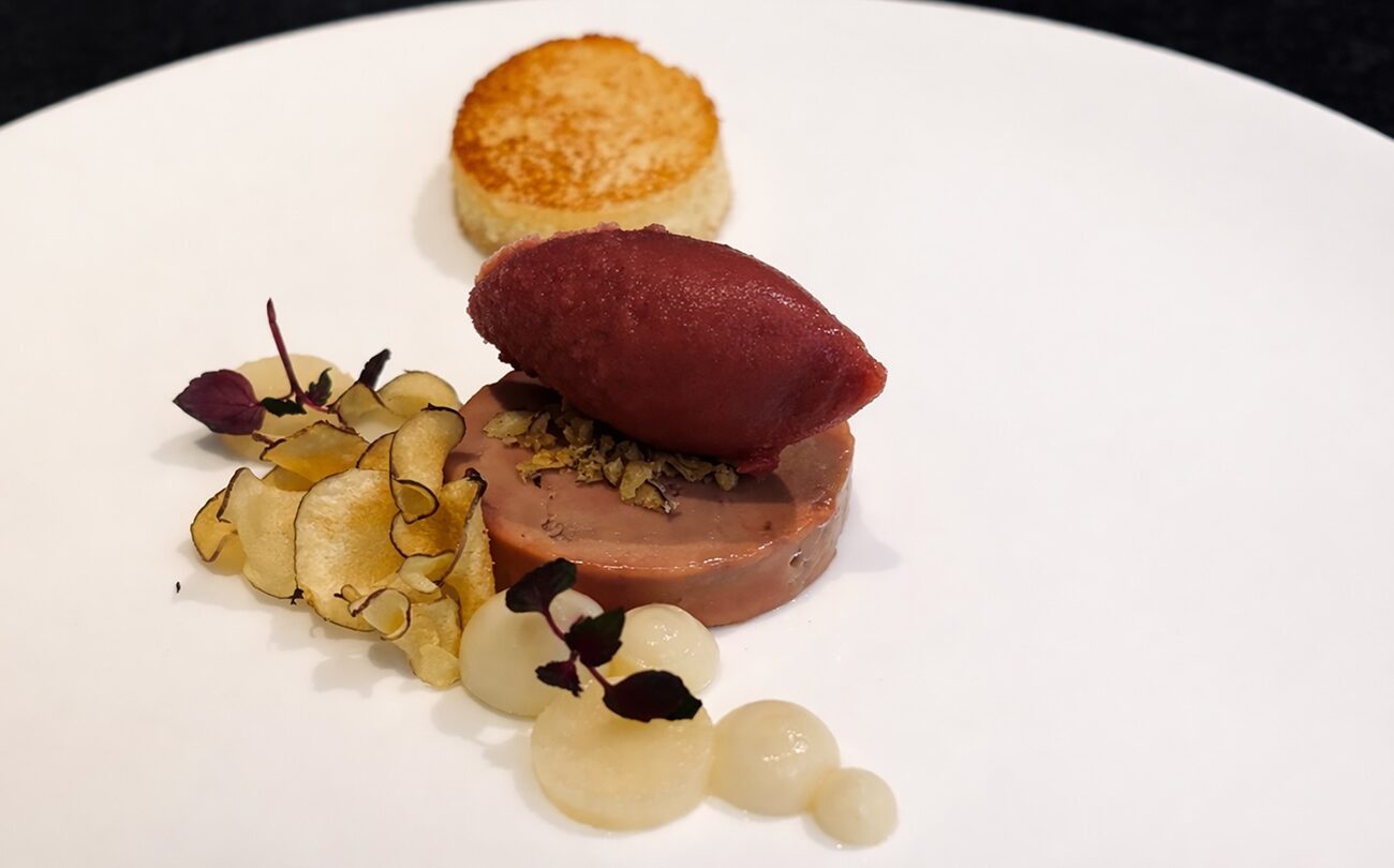 Runde Pâté-Scheibe mit rotem Sorbet, Chips und Toast auf weißem Teller