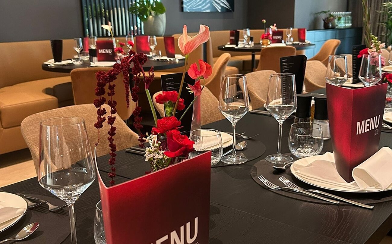 Menükarte (TEXT: MENU) steht auf gedecktem Tisch mit Blumen im Restaurant