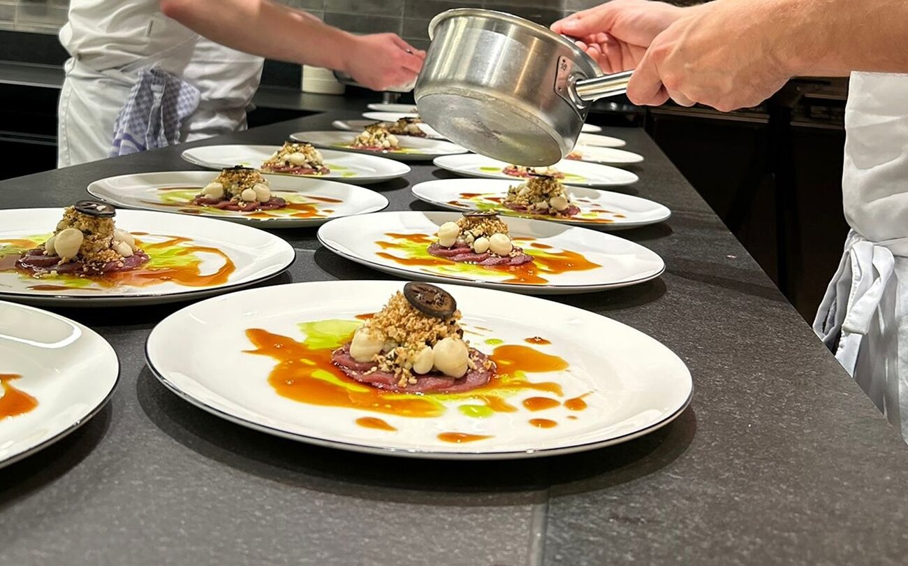 Garnierte Teller, Koch gießt Sauce auf mehrere Teller in Großküche