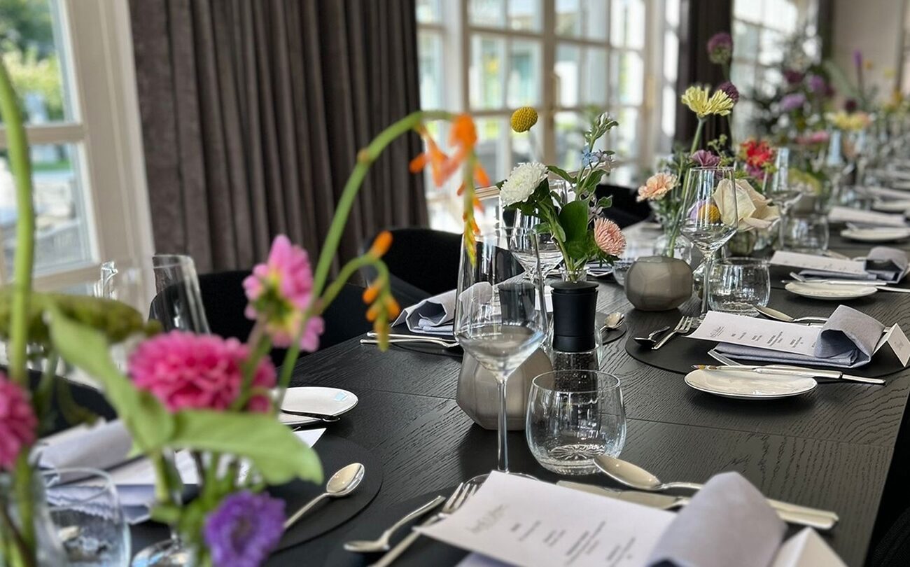 Gedeckter Tisch mit Blumen, Gläsern und Menükarten am Fenster